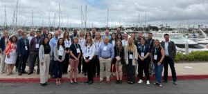 a group photo of people standing with sailboats in the background