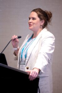 Jen Palumbo at a podium wearing a white blazer