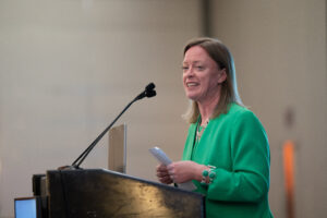 woman at a podium, she is wearing an emerald green suit